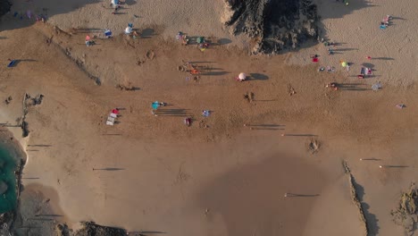 summer scene directly above people walking, resting, relaxing and enjoying calheta sandy beach, coastline, and ocean sea water and waves at sunset, madeira, portugal, overhead aerial static