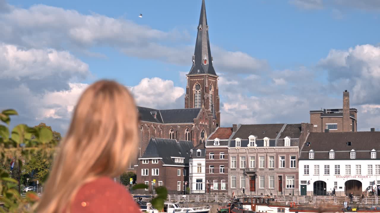 Woman standing on the riverbank in Maastricht, Netherlands, with the striking Sint-Martinuskerk (St. Martin's Church) as a prominent feature in the background
