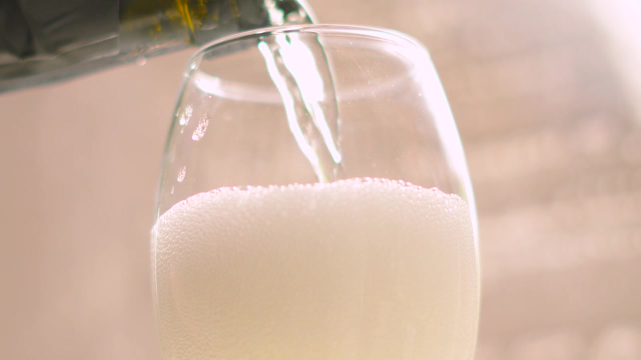 Elegante vertido a cámara lenta de champán frío en una copa flauta. Bebida de vino espumoso alcohólico francés servida en eventos de celebración. Iluminación natural. 4K.