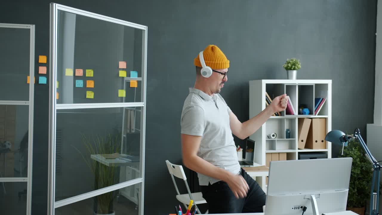 Joyful businessman dancing in office listening to music through headphones having fun in workplace