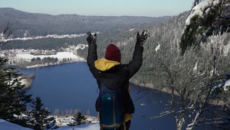 a young woman celebrates reaching the viewpoint over longemer lake in the vosges mountains