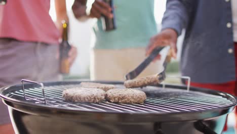 Happy-diverse-male-friends-barbecuing-and-drinking-beer-in-garden-on-sunny-day