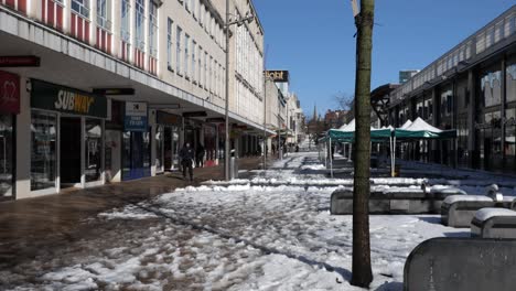 a snowy, sunny pedestrian highstreet as people browse the shops on a beautiful sunny day