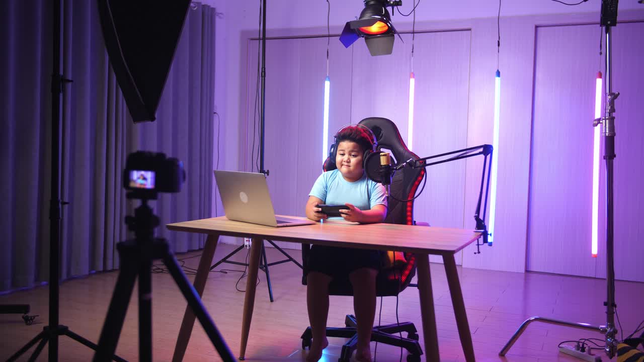 Asian Little Boy Playing Video Game With Mobile Phone Then Smiles To Camera While Live Stream, Professional Light Equipment