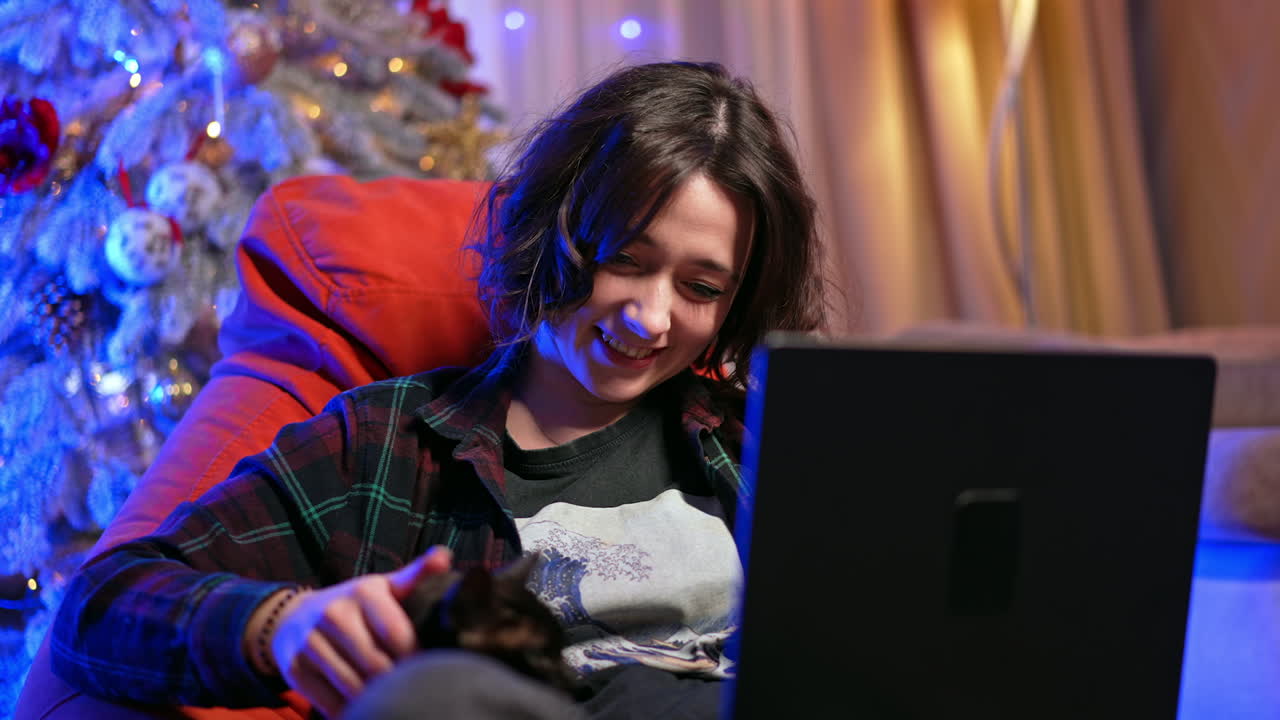 Young adult with laptop in winter. A person sits comfortably in a cozy chair, using a laptop, surrounded by festive decorations in a warm atmosphere