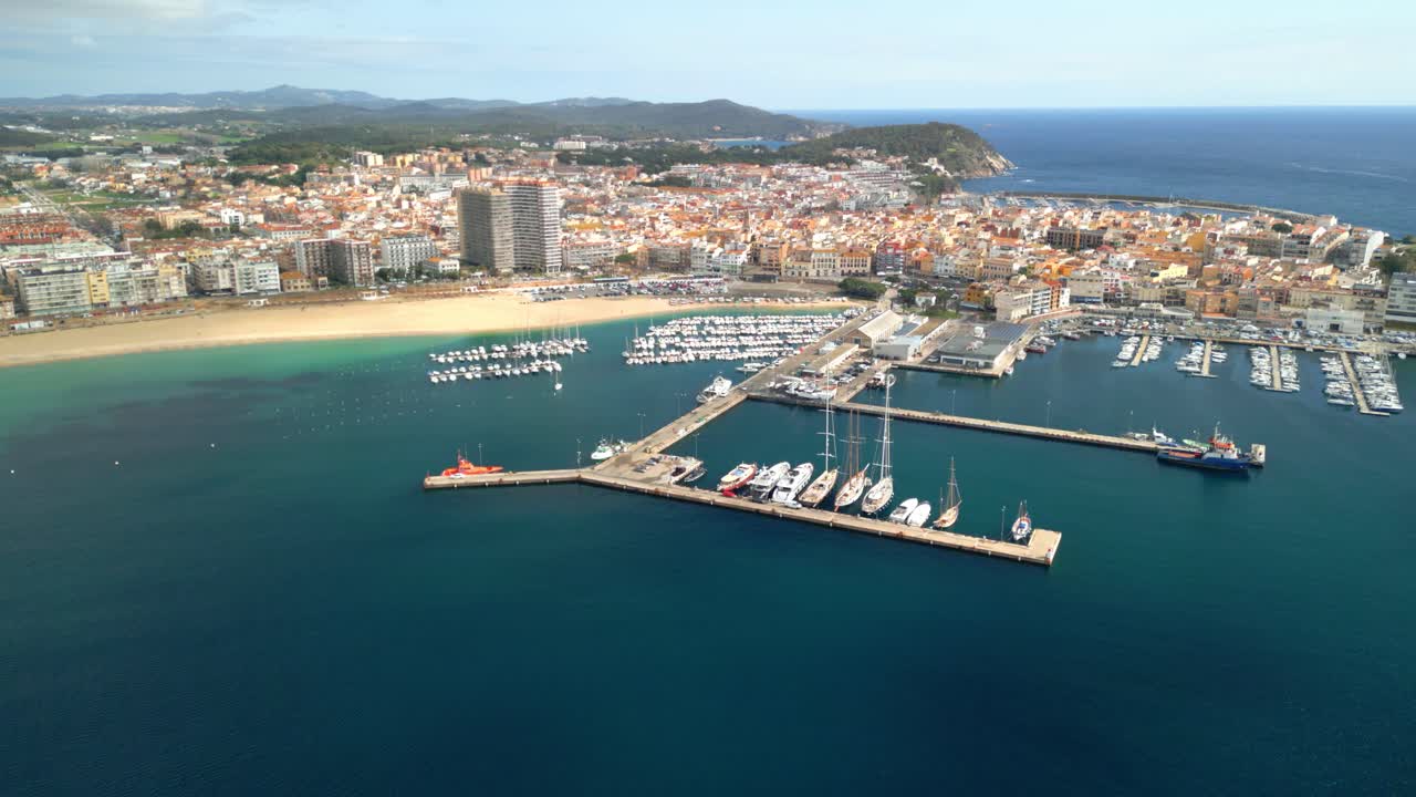 Palamos harbor and beach aerial view, located in costa brava, spain, shows many boats and yachts moored in the harbor, with the town visible in the background