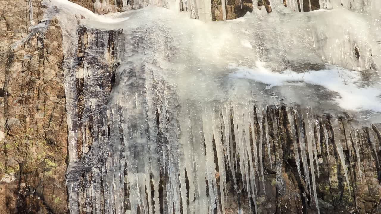 Many crowded massive icicles melting in the spring sun on a mountainside in clear blue sky. Video shot at 60fps, this video is 23,976 slowmotion so you can decide how you want it