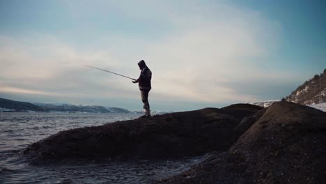 Man-Standing-On-A-Rock-And-Fishing-In-Trondheimsfjord-On-Cloudy-Winter-Day