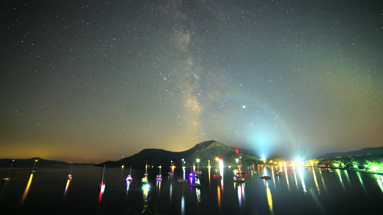 夜、ライトアップされたボートの上空に広がる天の川銀河