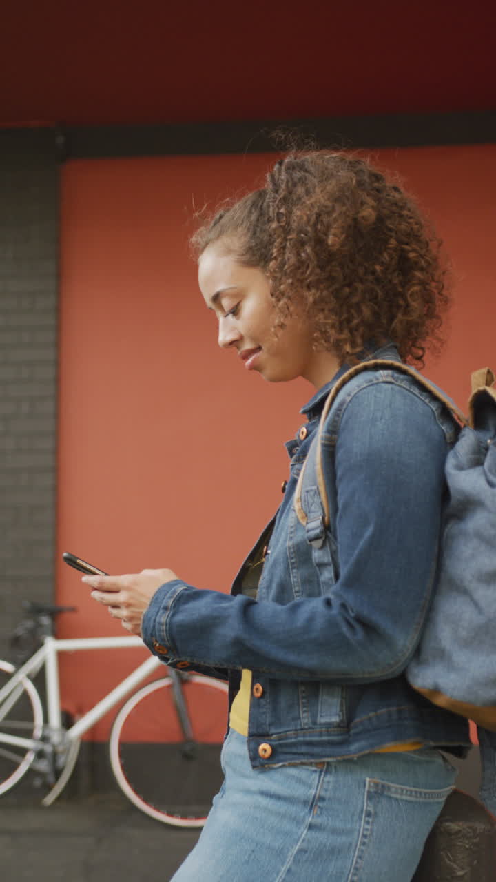 video vertical de una feliz mujer afroamericana usando un teléfono inteligente en la ciudad