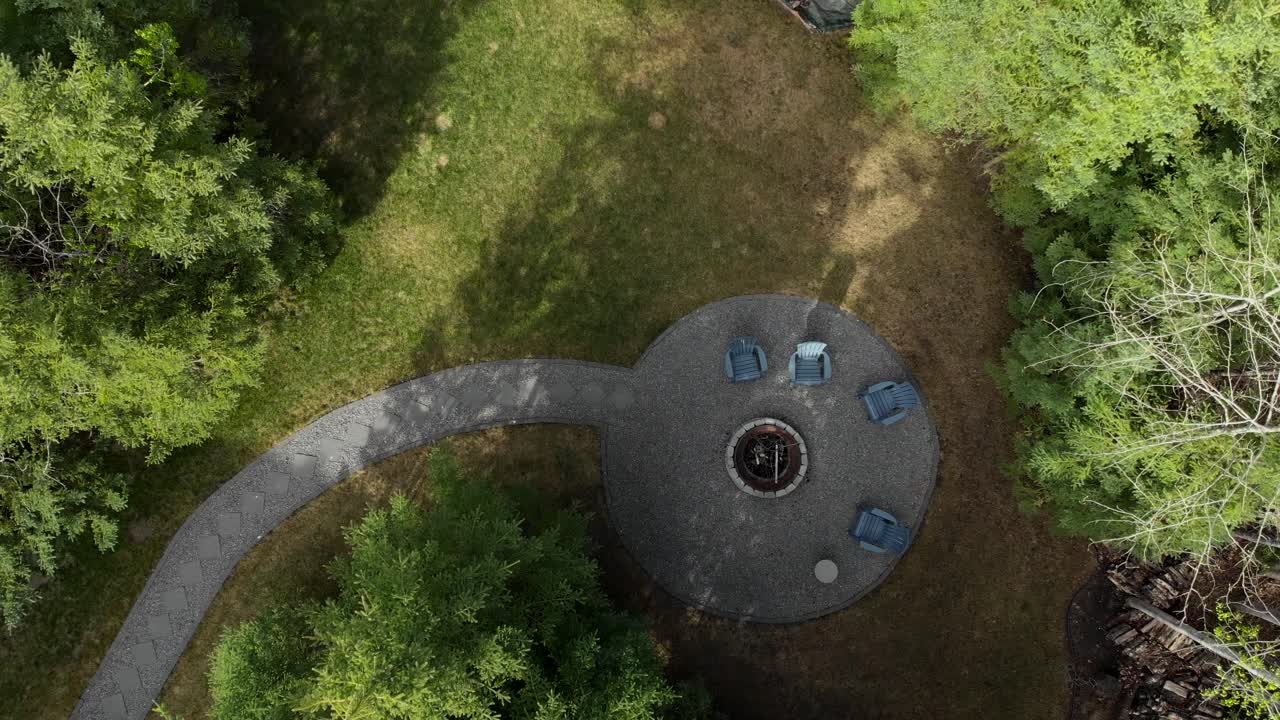 An amazing top down drone shot pulling away and rotating as it gets higher and higher above the beautiful yard, with a stone pathway leading up to a fire pit