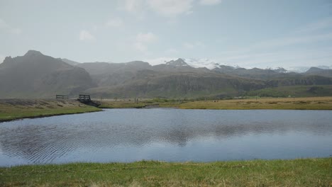 Ein-Ruhiger-Bergsee-An-Einem-Sonnigen-Tag-Mit-Schneebedeckten-Bergen-Am-Horizont