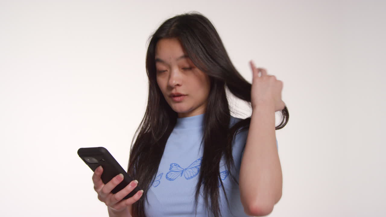 색 스튜디오 배경 앞에 드폰을 들고 있는 젊은 여성이 사진 부스 스타일의 초상화를 위해 포즈를 취하고 있다.