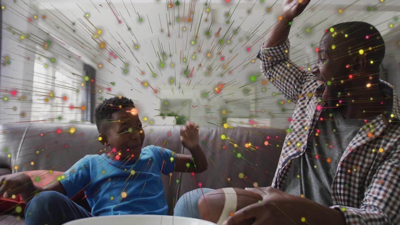 Father and son reacting to confetti and celebrating football win on couch, showcasing technology