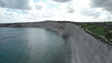 Drone-View-Over-Ras-il--Fenek-Limestone-Cliff-Side,-With-Tropical-Turquoise-Water,-Blue-Sky-And-Fluffy-White-Clouds,-Malta