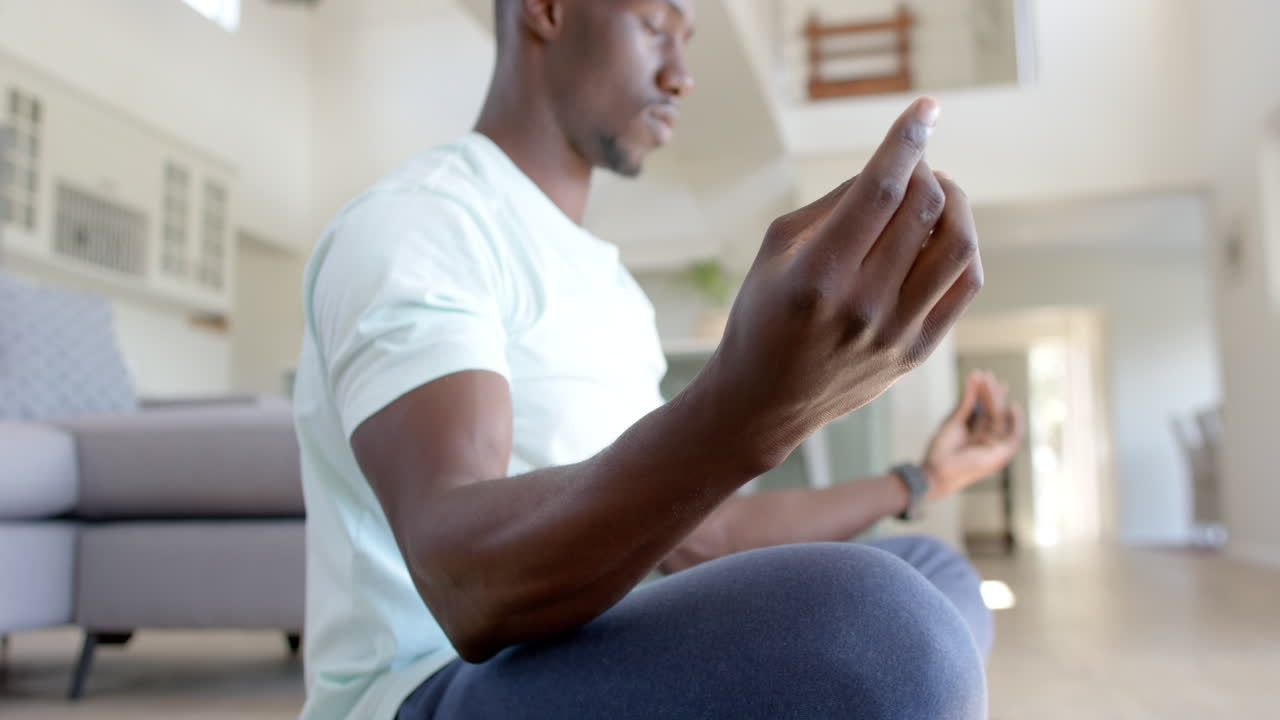 Focused african american man practising yoga meditation in sunny living room, slow motion