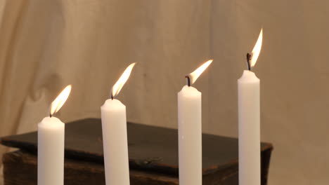 slow panning shot of four candles by old heavy book, windy conditions