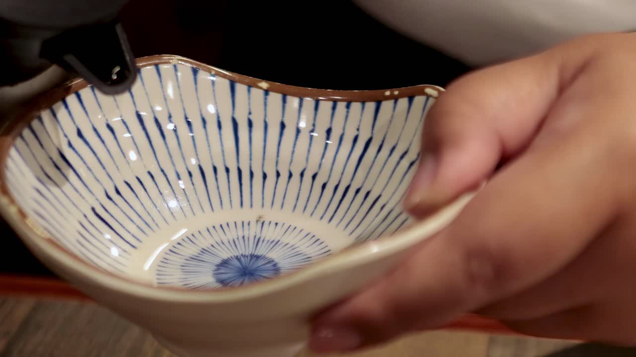 Close-up of liquid being poured into a decorative ceramic bowl held by a hand.