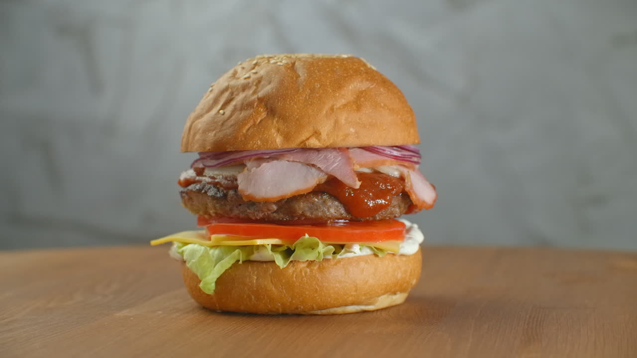 gran hamburguesa con carne de res, chuleta, tomates, setas y pepinos con queso derretido gira en una tabla de madera sobre un fondo claro.