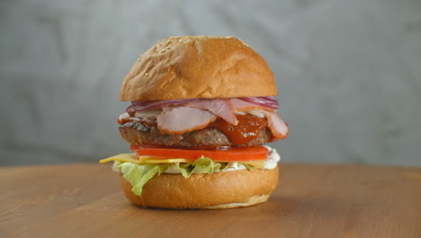 Great-Burger-with-beef-cutlet-tomatoes-mushrooms-and-cucumbers-with-melted-cheese-rotates-on-a-wooden-Board-on-light-background.