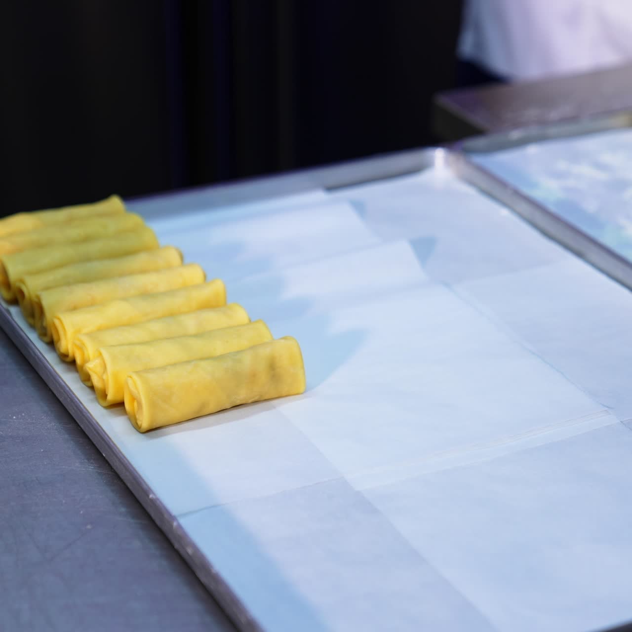 Hands in black latex gloves put the rolled crepes with stuffing on a tray. Preparing fresh food at restaurant. Close up