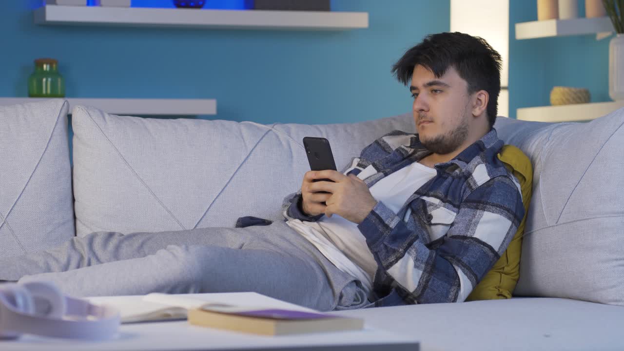 소파에 누워 있는 남자가 전화를 사용하고 있습니다. 쾌적하고 편안한 자세입니다.