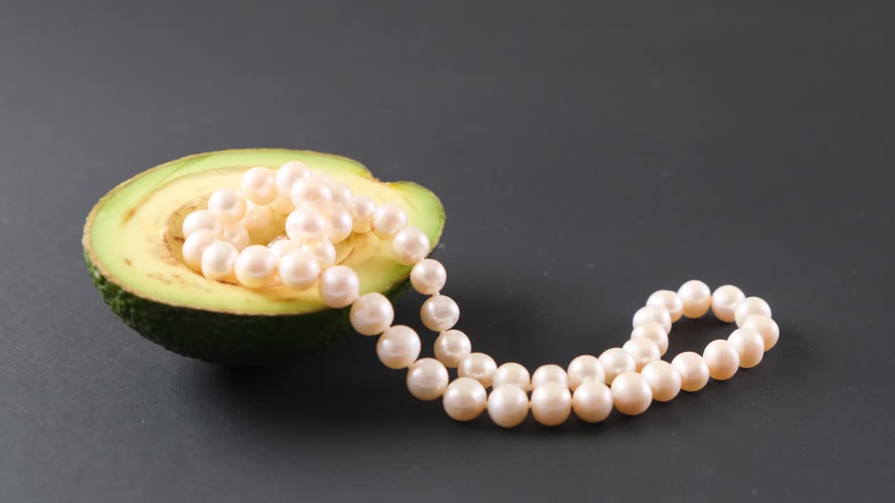 검은 바탕에 진주와 함께 아보카도 반. 초현실주의. 패션 음식 디자인.