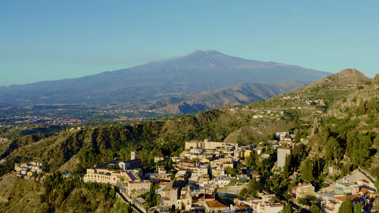 Luftfoto af italiensk by omgivet af frodige bjerge. Udsigt til Europas mest aktive vulkan Etna fra Taormina. Et vartegn på Sicilien.