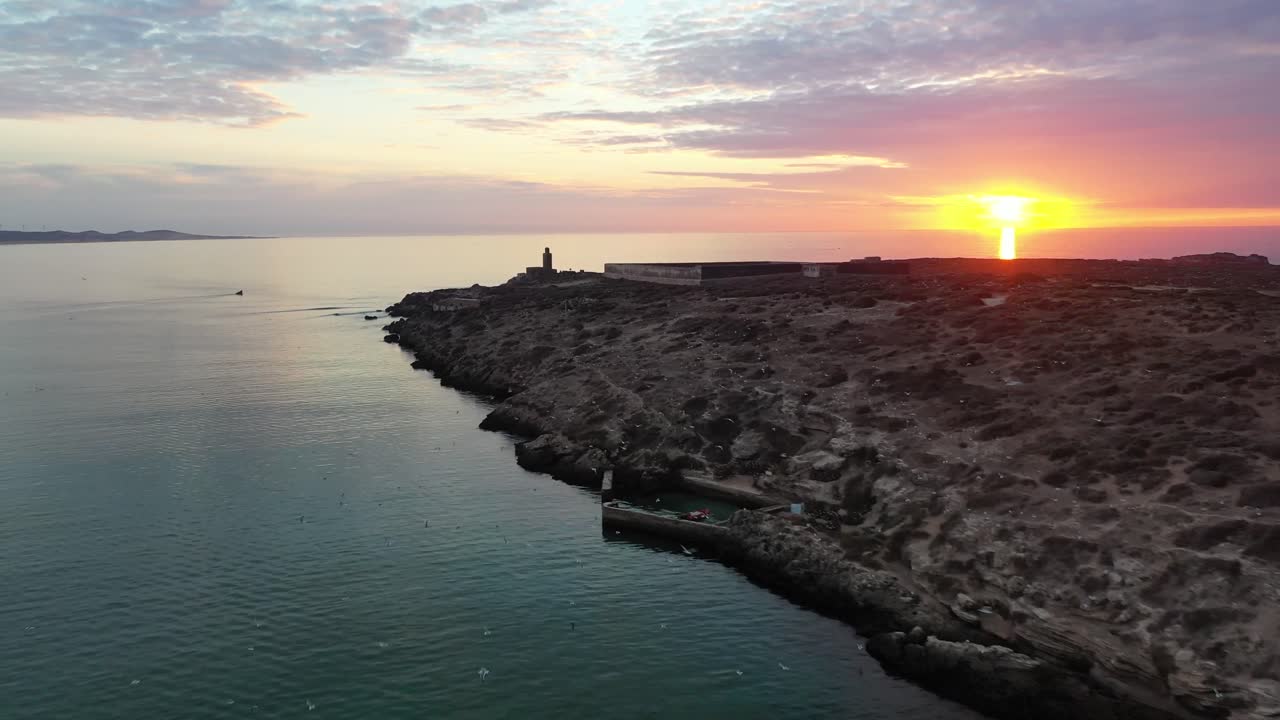 Plano cinematográfico com drone capturando a silhueta escura do minarete de uma mesquita e edifícios antigos da cidade em Essaouira, Marrocos, contra um céu vibrante de pôr do sol, repleto de nuvens altocumulus texturizadas (céu mackerel).