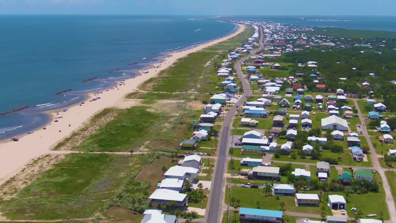 Forward-moving aerial footage over Grand Isle, Louisiana, reveals beaches, green spaces, LA-1 roadway, restaurants, coastal homes, and a scenic view of Caminada Bay beyond the barrier island