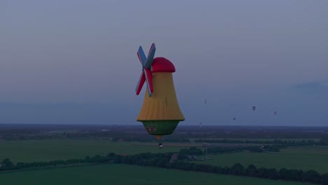 Aerial-view-of-colorful-hot-air-balloon-in-windmill-shape-at-sunset,-Netherlands