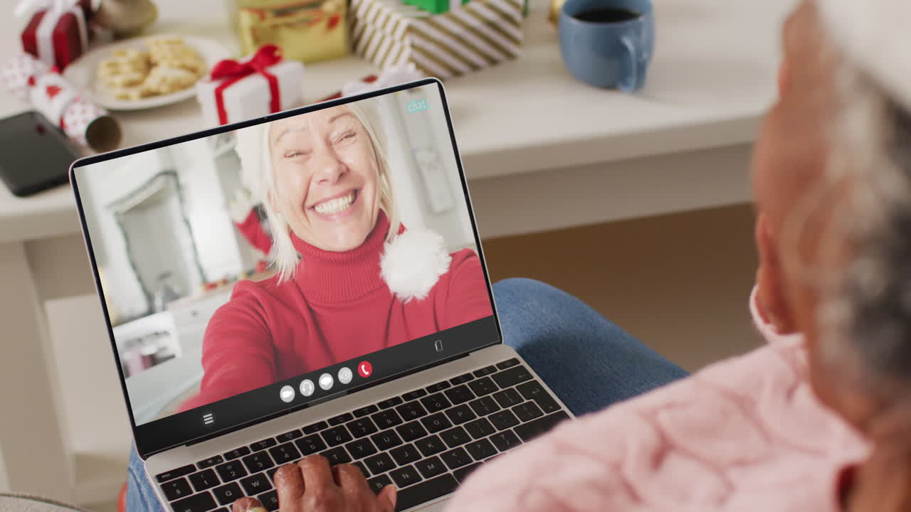 animación de una mujer afroamericana en el sombrero de santa en una llamada de video portátil con una mujer en navidad