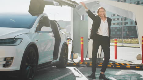 mujer cargando un ev en una estación de carga y emocionada