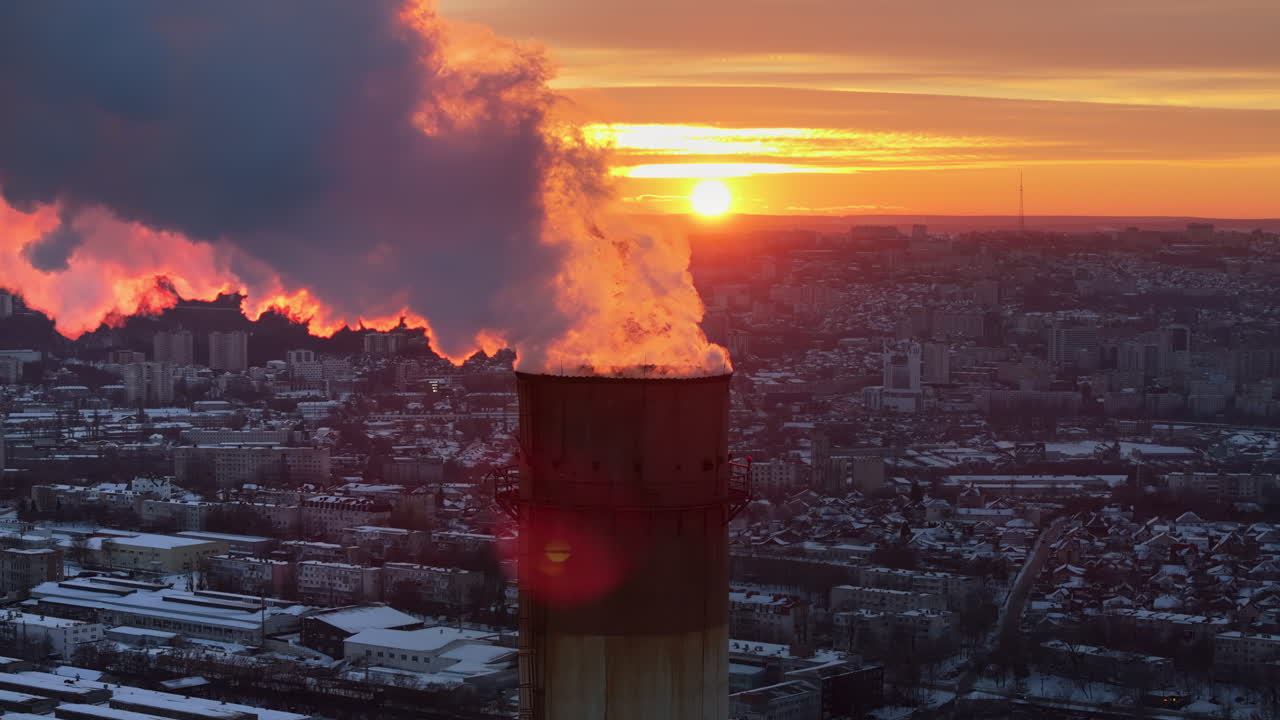 Aerial drone view of a working thermal power station in Chisinau at sunset. City covered in snow. Steam and smoke coming from pipes. Moldova