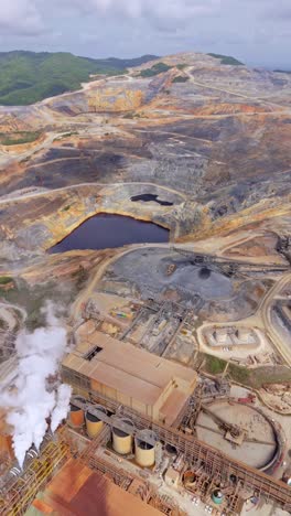 drone flying over industrial buildings, tanks, and steam emissions at barrick gold mine, landscape, dominican republic. aerial forward, vertical format