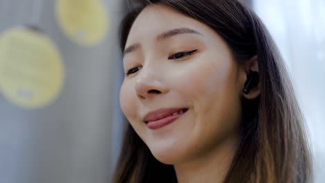 close up asian woman wearing wireless in-ears headphones listening to music sitting on the table at home