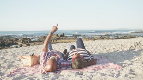 happy senior african american couple lying on blanket at beach, slow motion