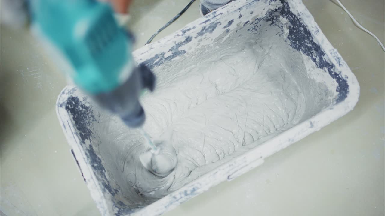 Mixing Construction Material: A Close-Up View of a Worker Using a Drill to Blend Cement in a Mixing Tub for Building and Renovation Projects