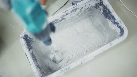 mixing construction material: a close-up view of a worker using a drill to blend cement in a mixing tub for building and renovation projects
