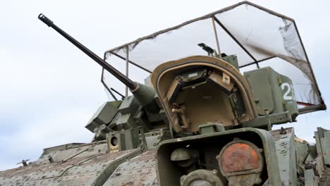a low-angle close-up of the 25mm bushmaster autocannon on a us-made m2 bradley ifv during a training exercise in ukraine. a 'cope cage' is visible above the turret