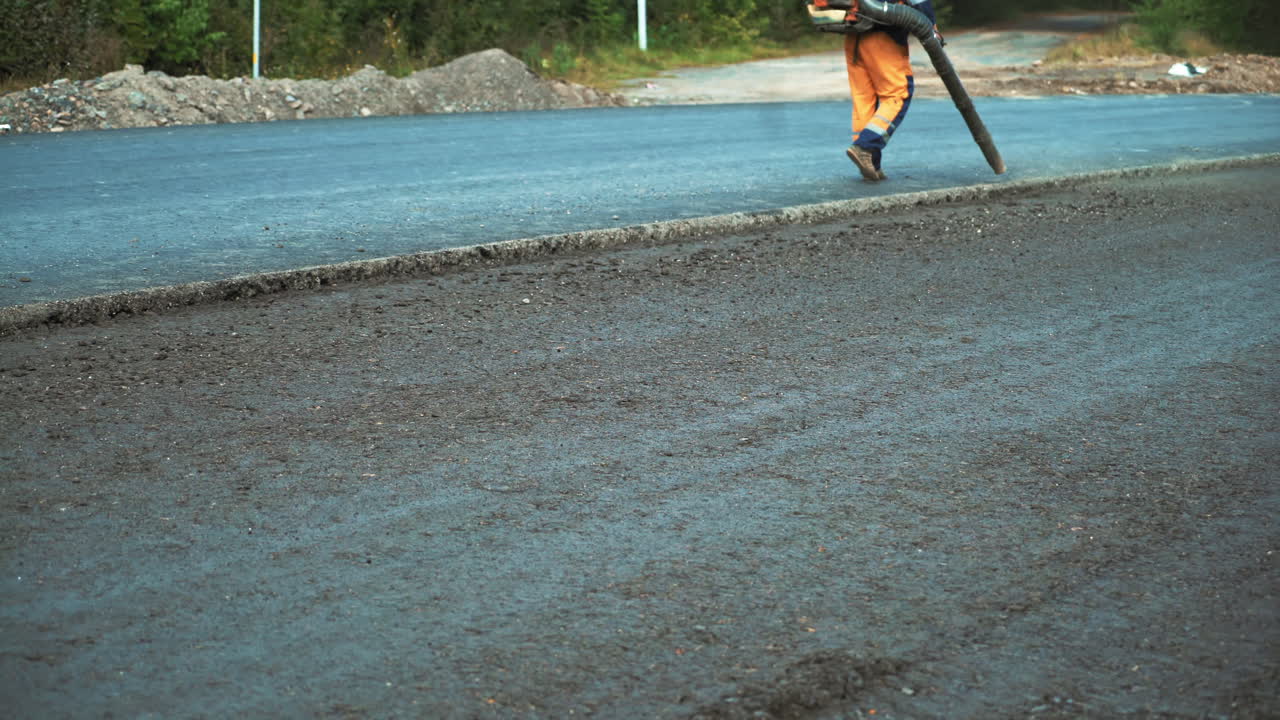 Preparation for a paving on the road. Worker is using compressed air to blow off dust and old asphalt particles from the road.