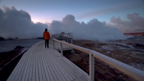 Person-Walking-On-The-Platform-At-Gunnuhver-Geothermal-Area-With-Steam-Vents-In-Iceland