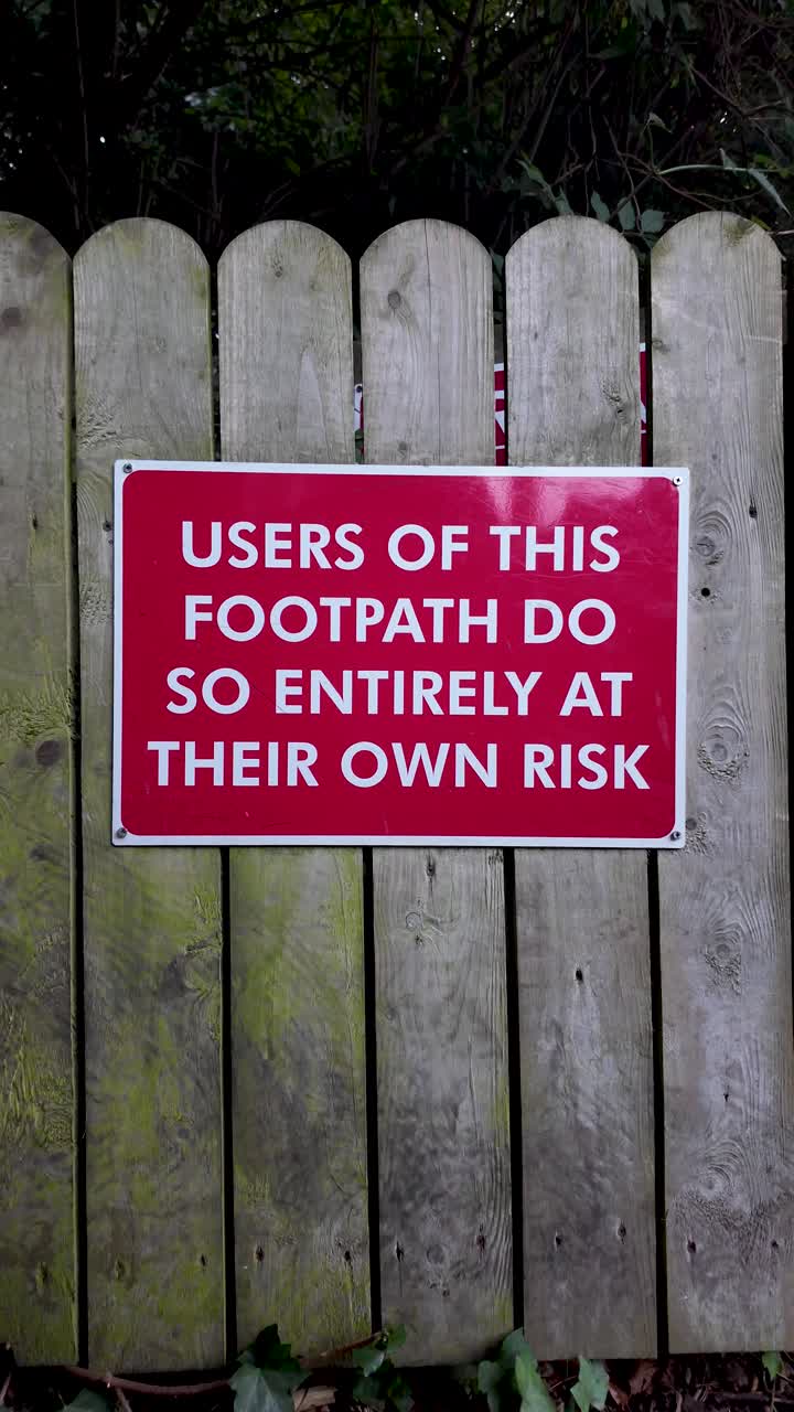 Red warning sign on weathered wood fence, alerting walkers to personal risk on the footpath. vertical video