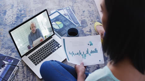 african american woman holding a document having a video call on laptop at home