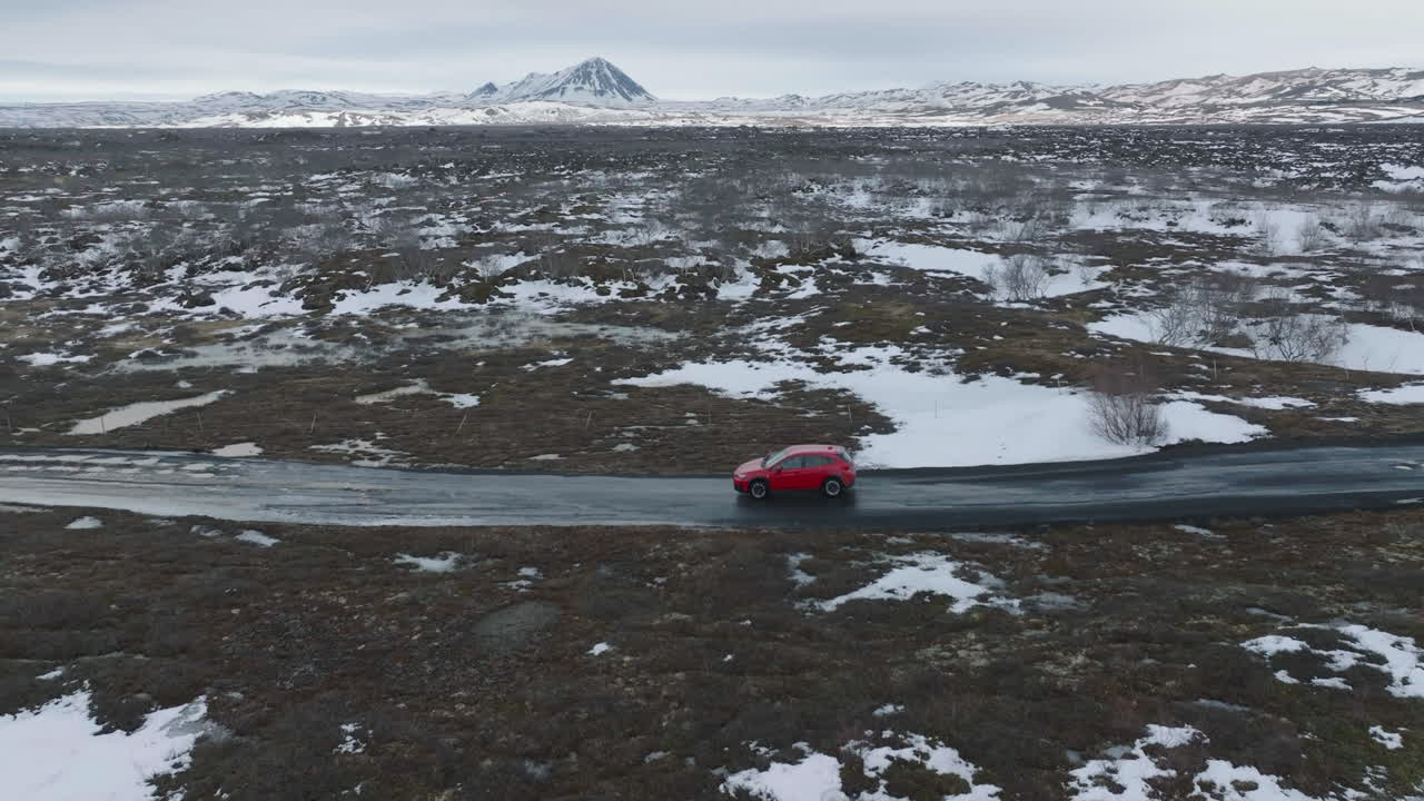 Aerial View of Red Car Moving on Wet Countryside Road in Scenic Landscape of Iceland, Late Winter Season