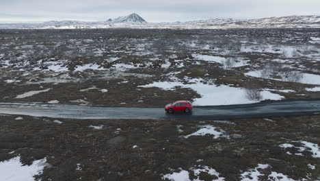 vista aérea de un coche rojo que se mueve en una carretera húmeda en el paisaje escénico de islandia, a finales de la temporada de invierno