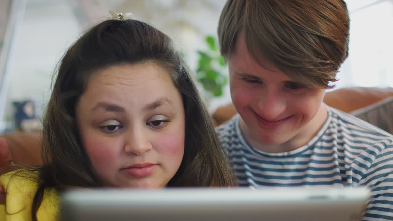 집에서 디지털 태블릿을 보는 소파에 앉아있는 젊은 다운 증후군 부부