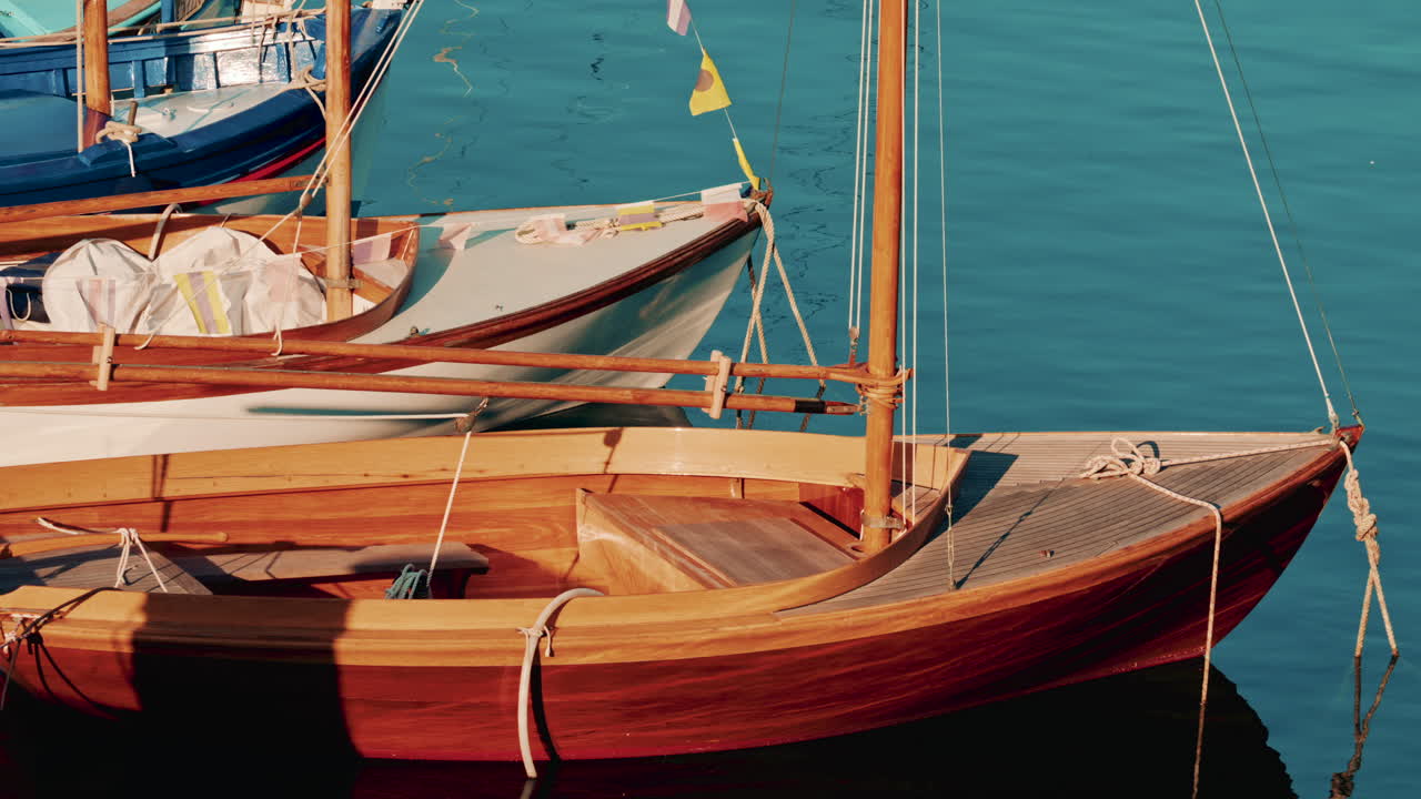 Two wooden sailboats docked on still turquoise water, glowing warmly under golden hour sunlight