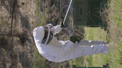 vertical, slow motion - beekeeper smokes beehives to prevent aggression, slowmo wide shot