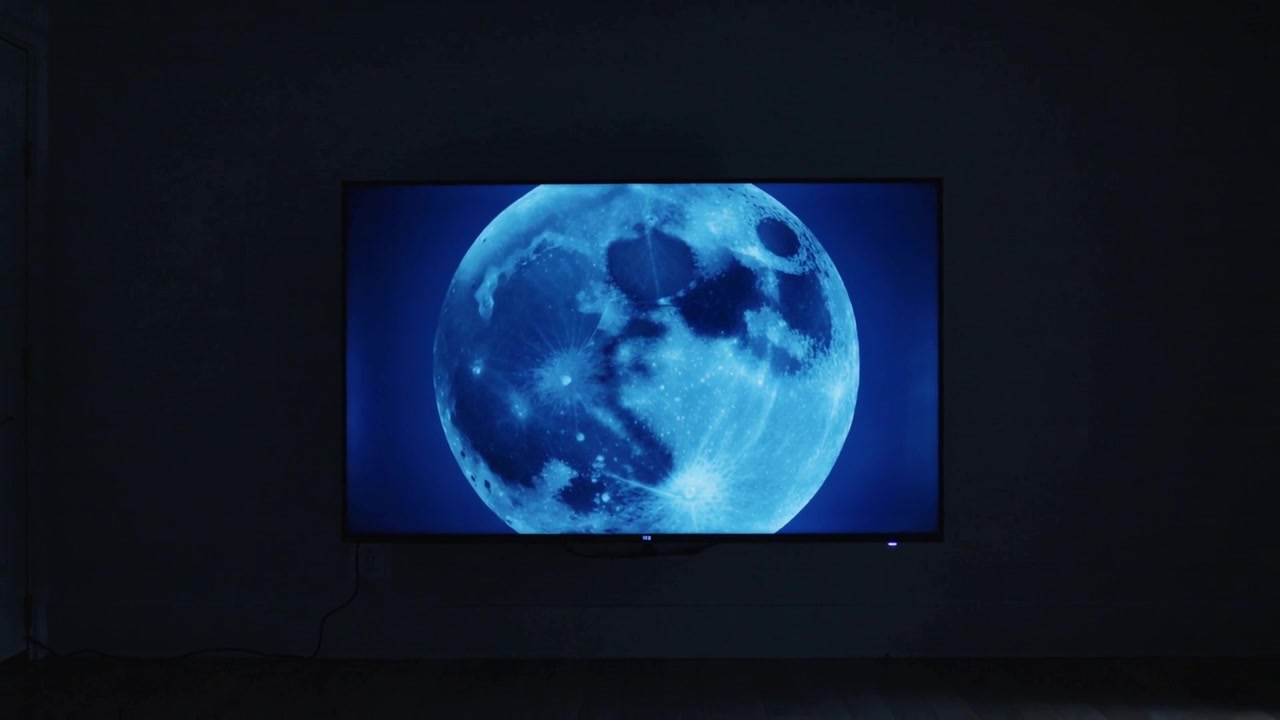 Schermo a parete che mostra una luna blu con un bagliore che cambia lentamente in una galleria in penombra, cavo visibile.